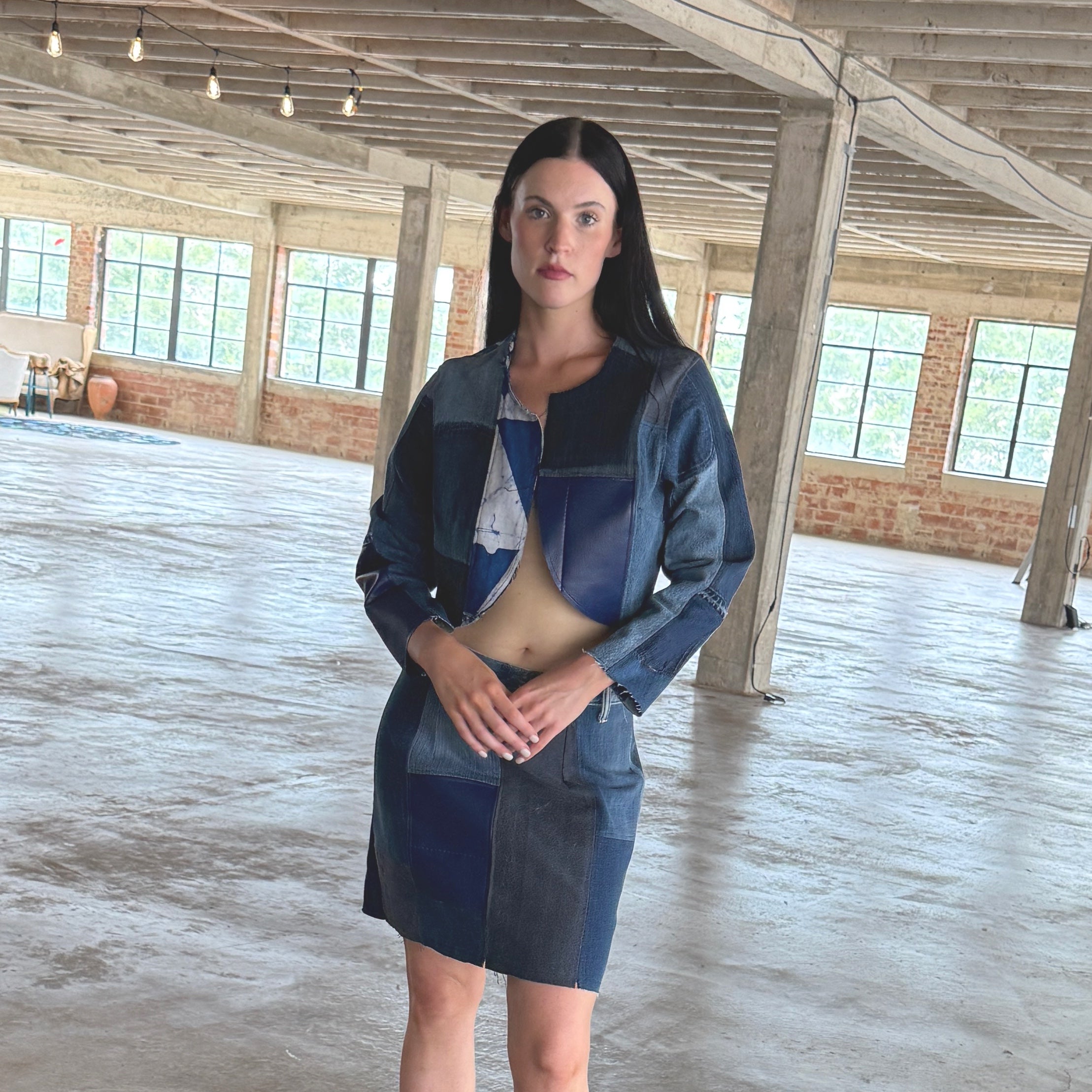 Woman in a blue outfit standing in a large, open industrial-style room with high ceilings and large windows.