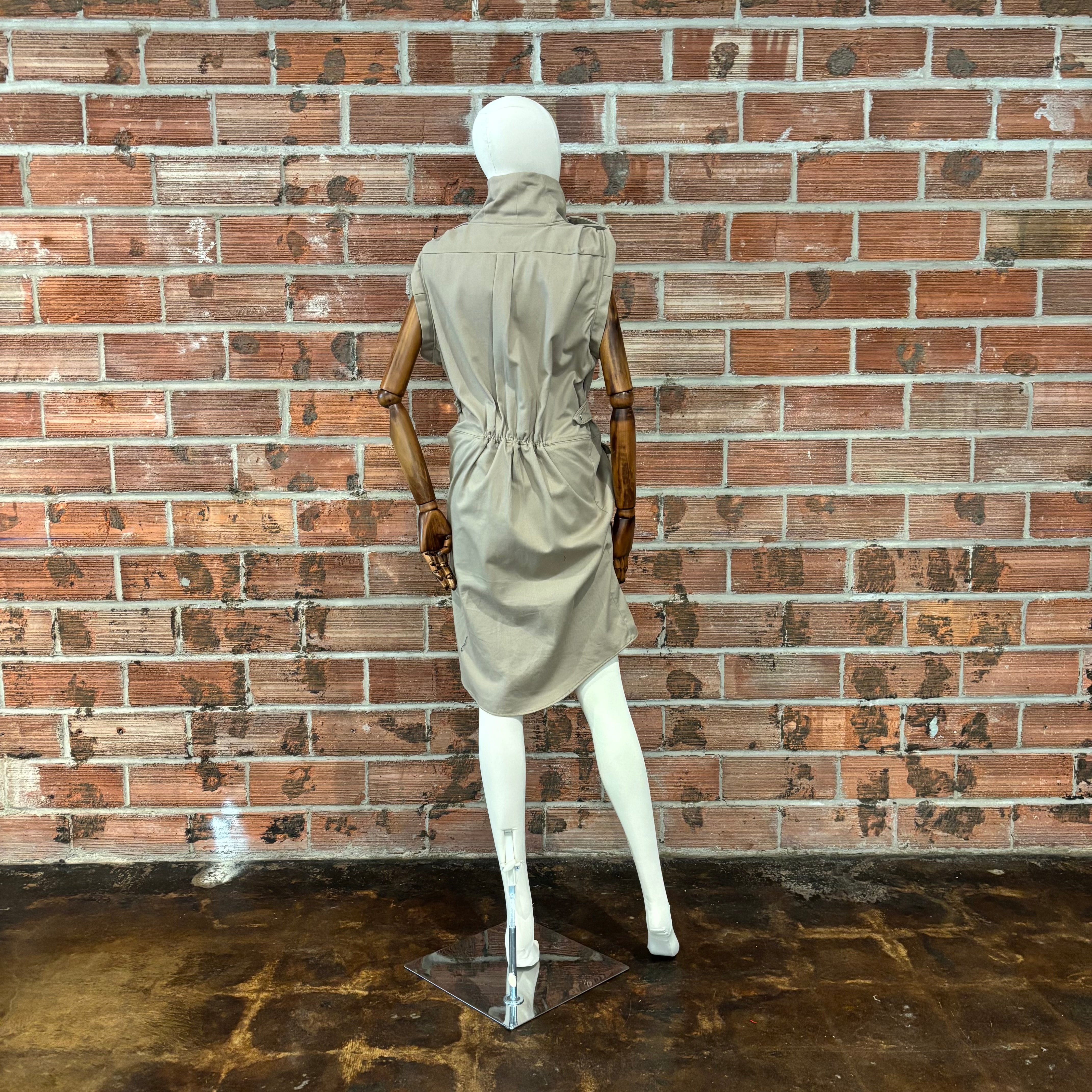 Mannequin wearing a beige dress against a brick wall.