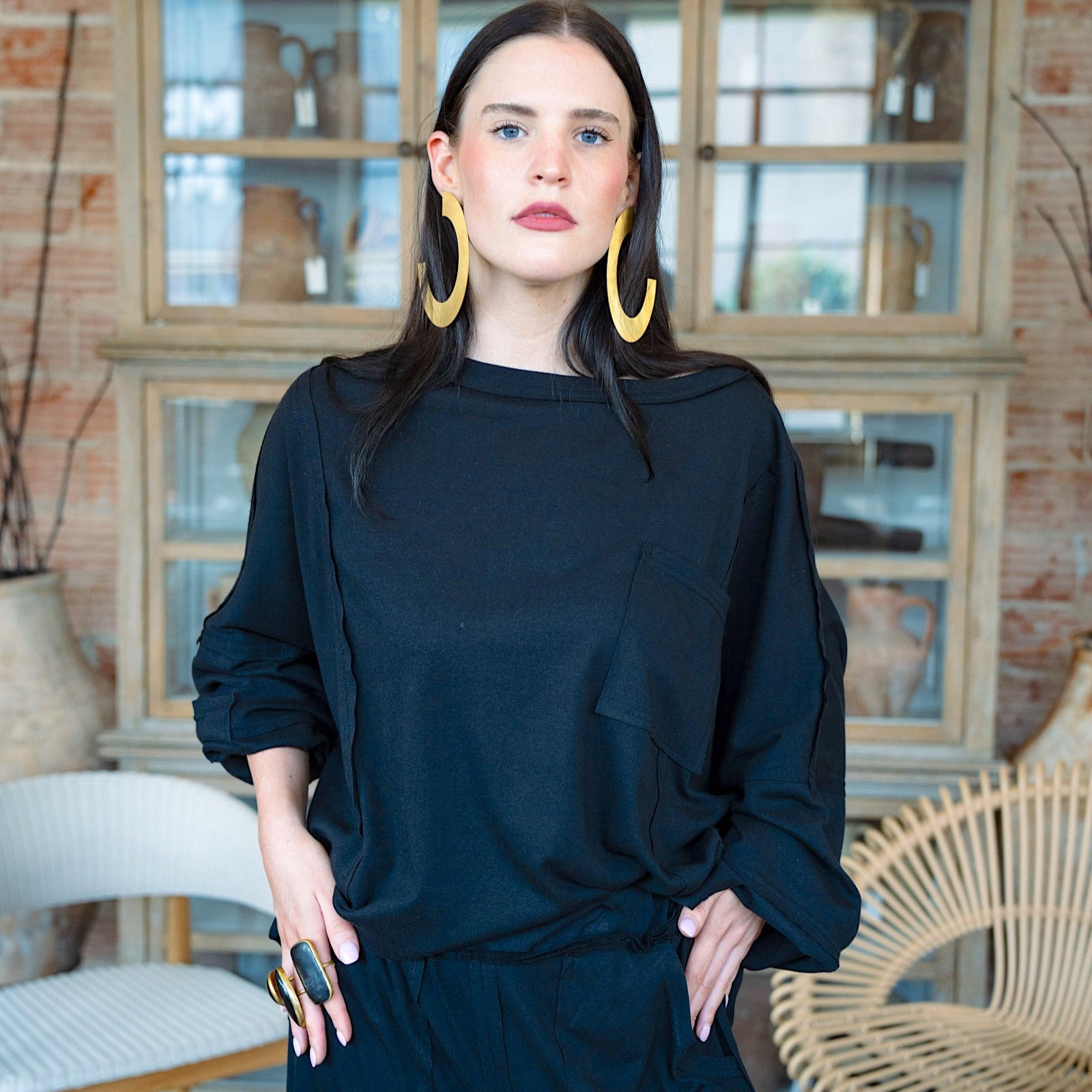Woman wearing a black outfit with gold earrings in a room with decorative vases and furniture.
