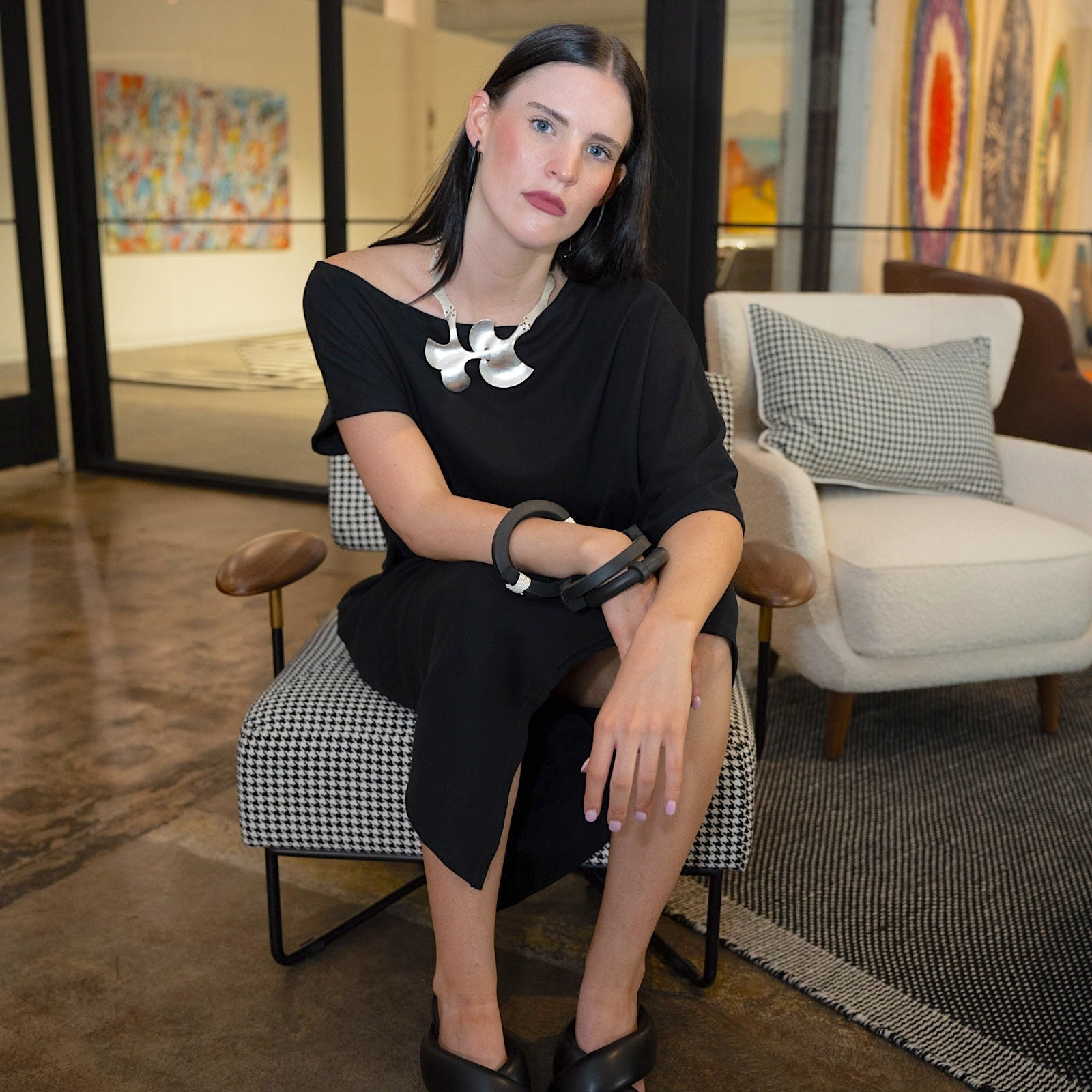 Woman in a black dress sitting on a chair in an indoor setting with modern decor.
