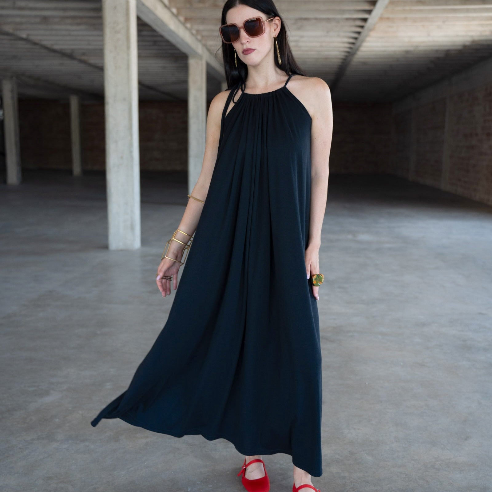 Woman in a black dress with red shoes standing in an industrial-style room.