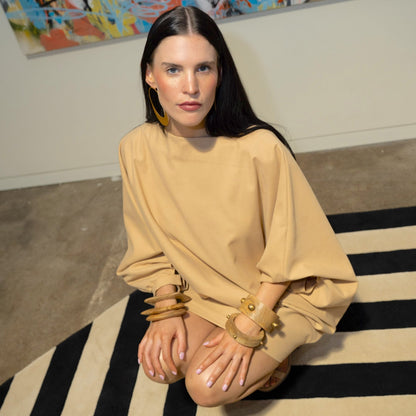 Woman in beige outfit sitting on a black and white striped rug with colorful abstract art in the background.