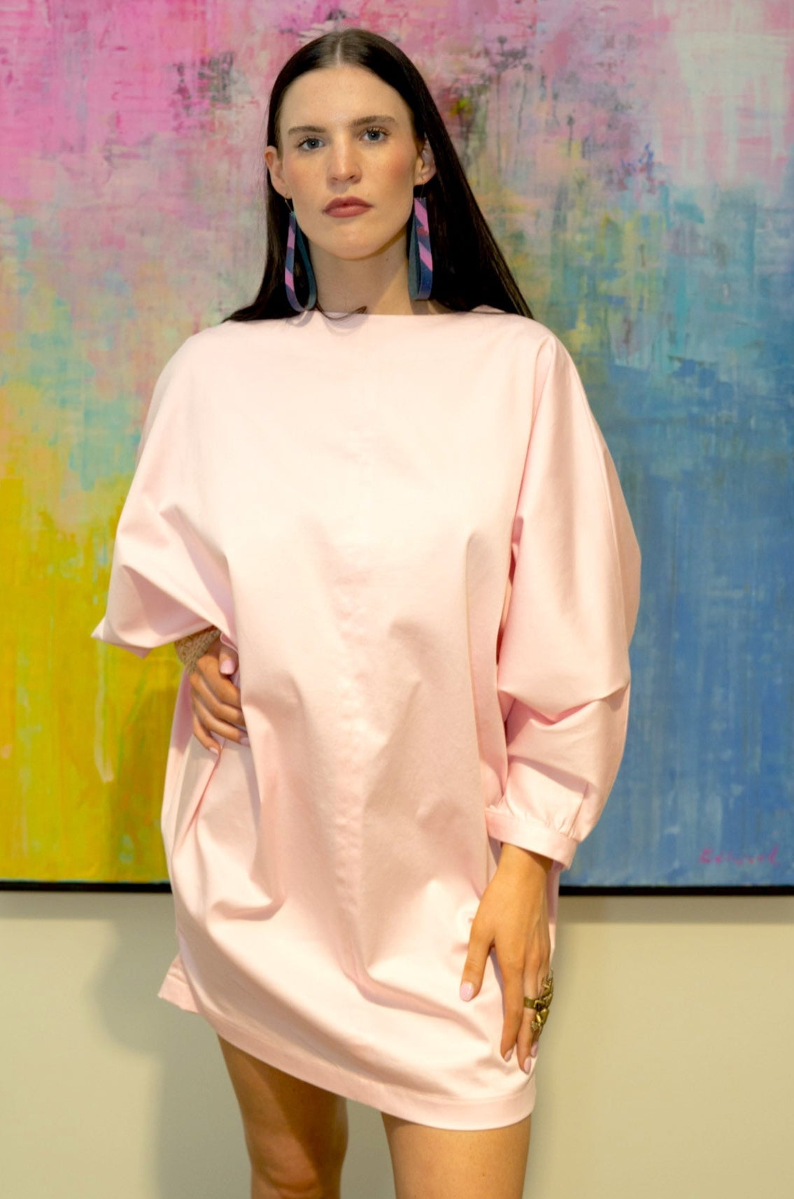 Woman wearing a pink dress standing in front of a colorful abstract painting.
