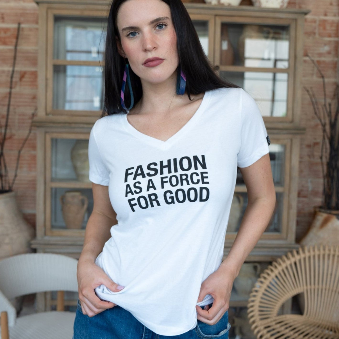 Woman wearing a white t-shirt with 'Fashion as a Force for Good' text in a room with decorative vases and furniture.