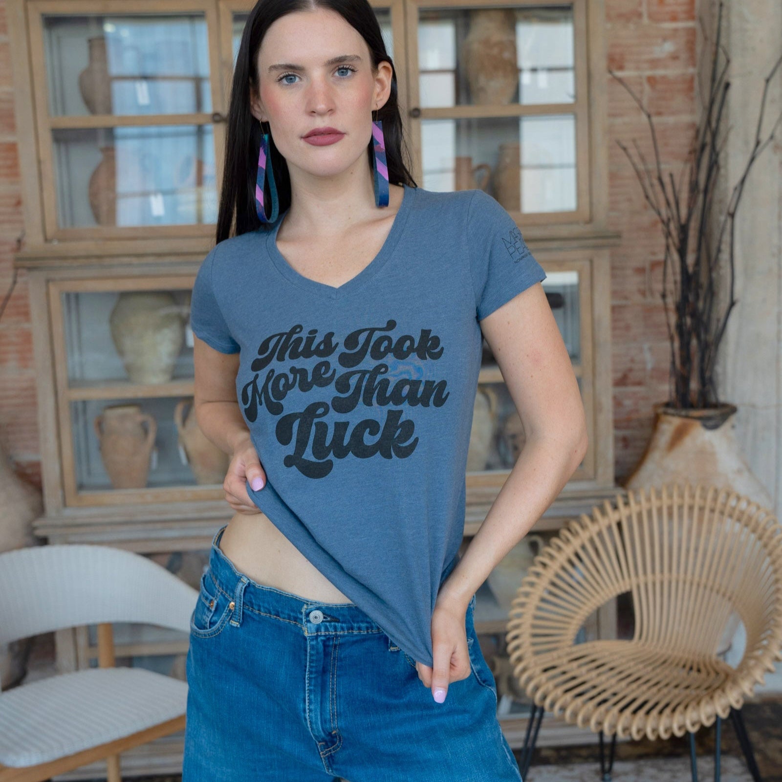 Woman wearing a blue t-shirt with text in a room with decorative vases and furniture.