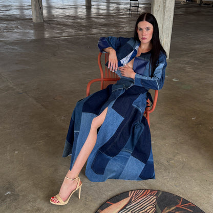 Woman sitting on a chair wearing a long, patchwork denim dress in an indoor setting.