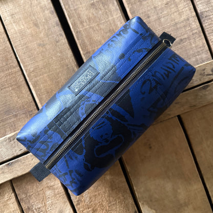 A blue zippered pouch with a black graphic pattern, resting diagonally on a rustic wooden plank surface.
