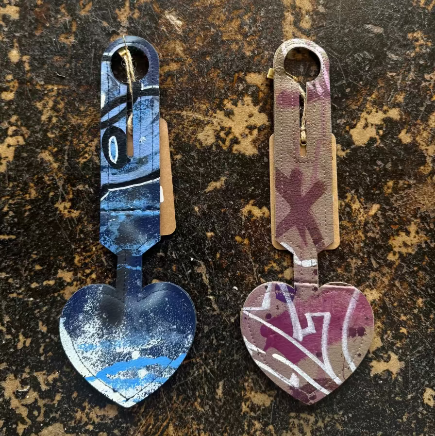 Two heart-shaped luggage tags with abstract graffiti on a leather surface