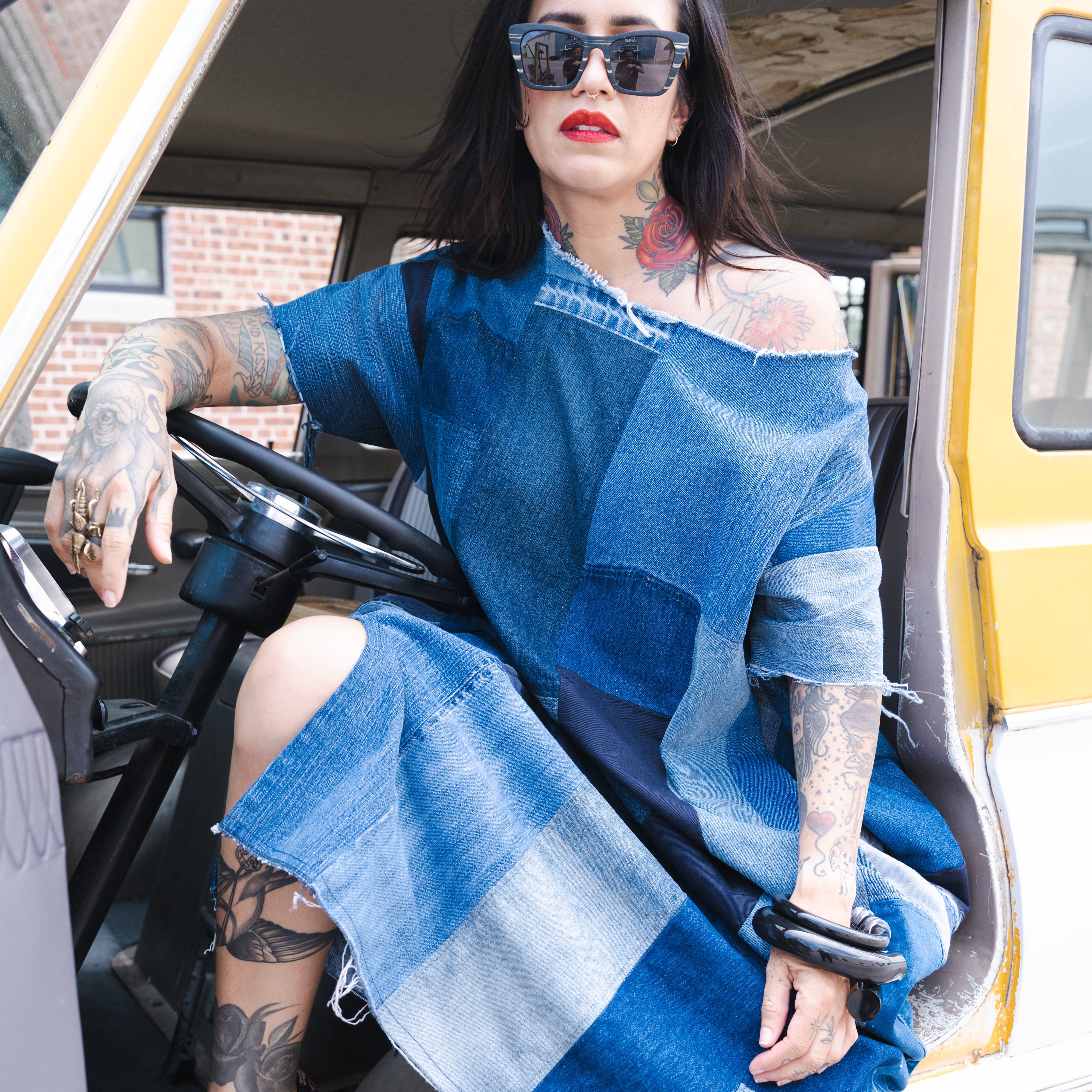 Woman in a blue up cycled denim dress sitting inside a yellow vehicle