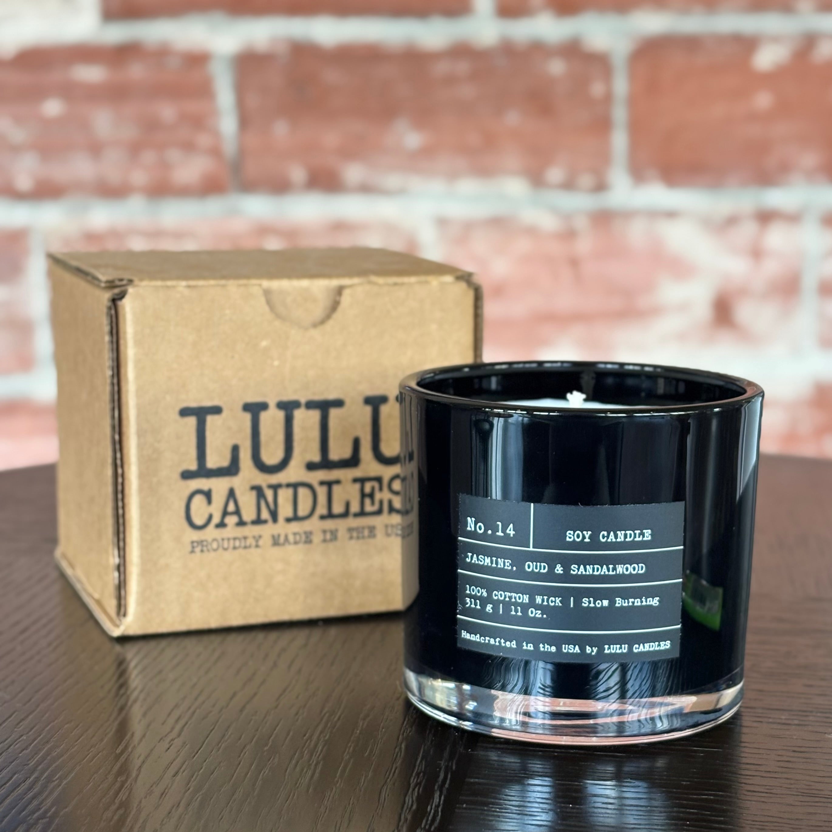 Black candle with label and Lulu Candles box on a wooden surface with brick wall background