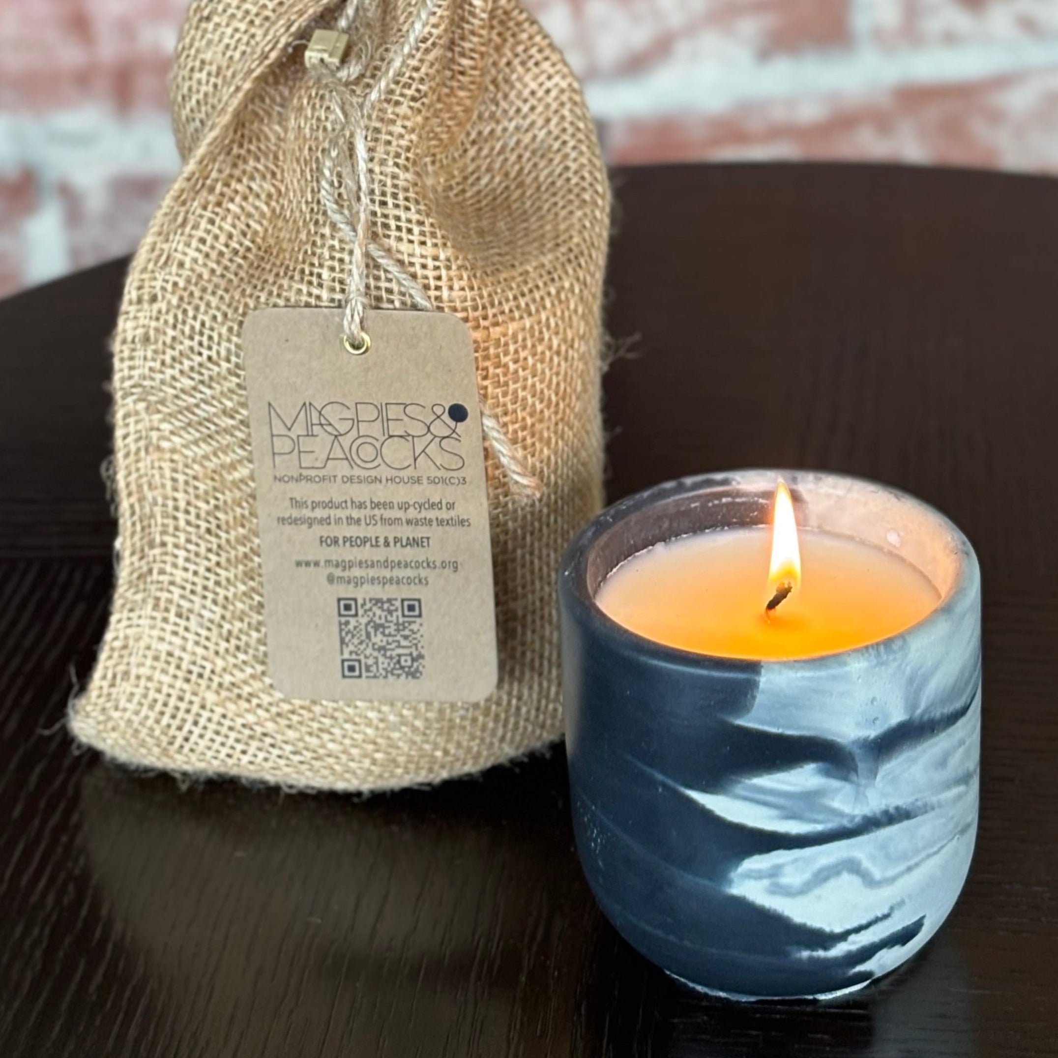 Candle in a marble container with a burlap bag on a dark surface.