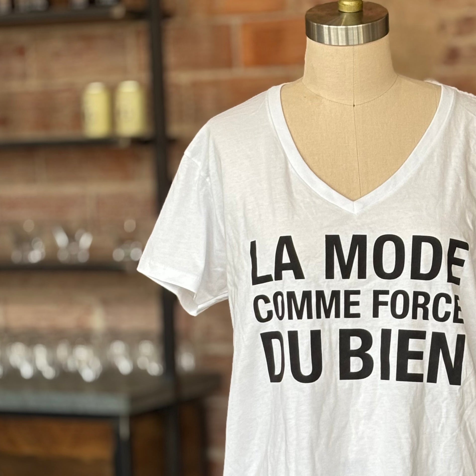White t-shirt with black text on a mannequin against a brick wall.
