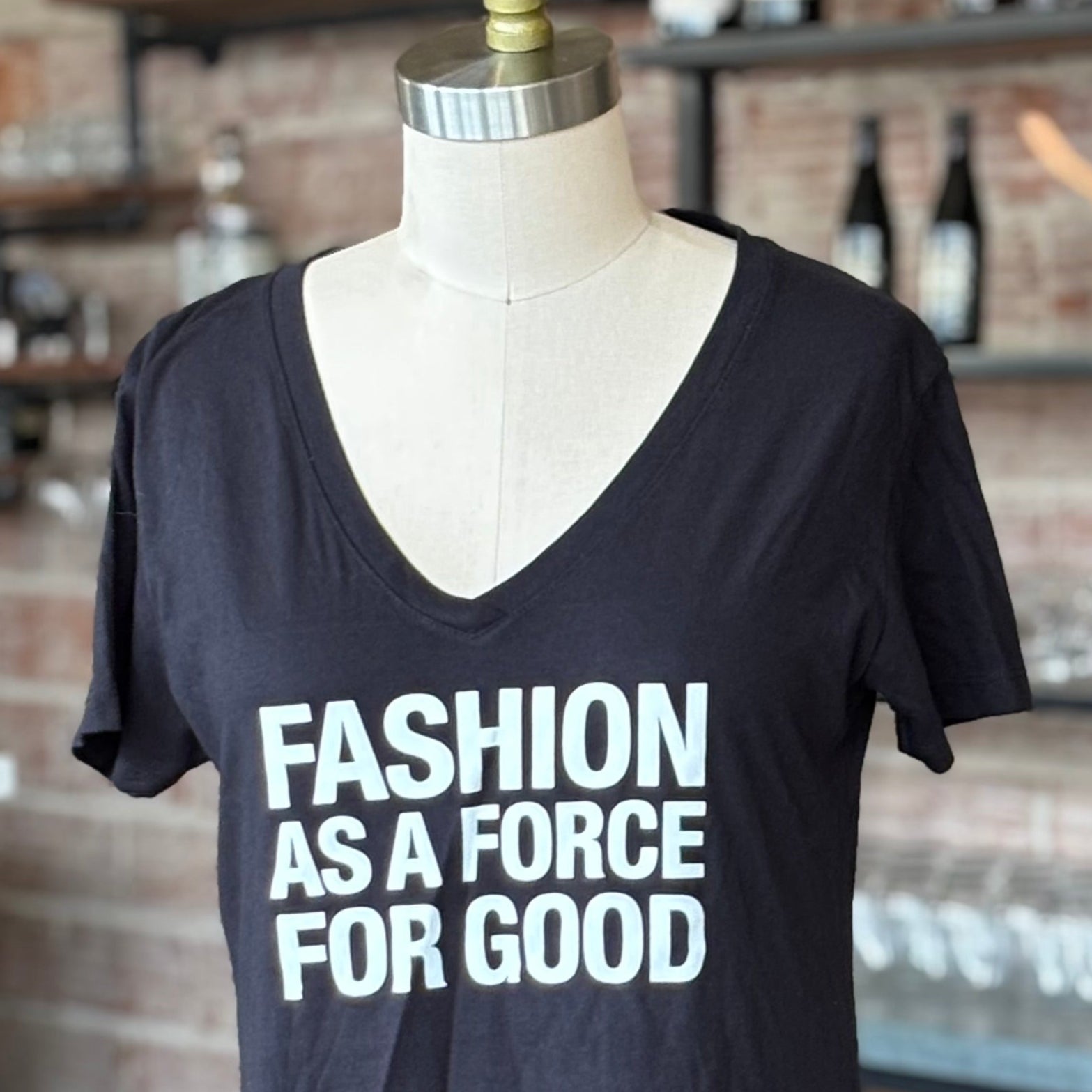 Black t-shirt with 'FASHION AS A FORCE FOR GOOD' text on a mannequin in a casual setting.