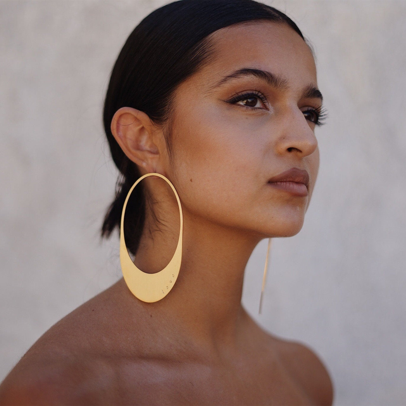Woman wearing a gold hoop earring against a neutral background